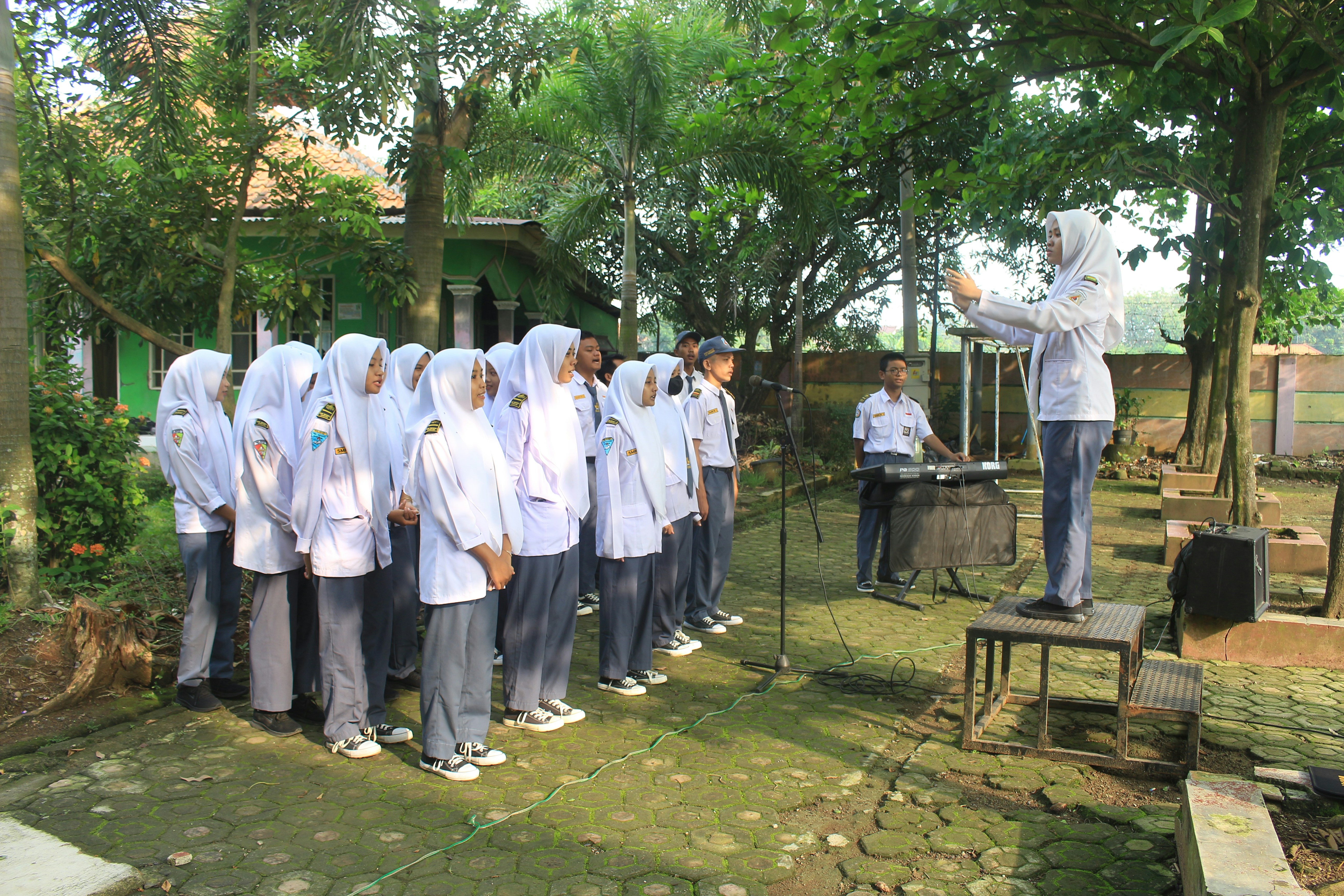 Students in uniform singing outdoors with a conductor.