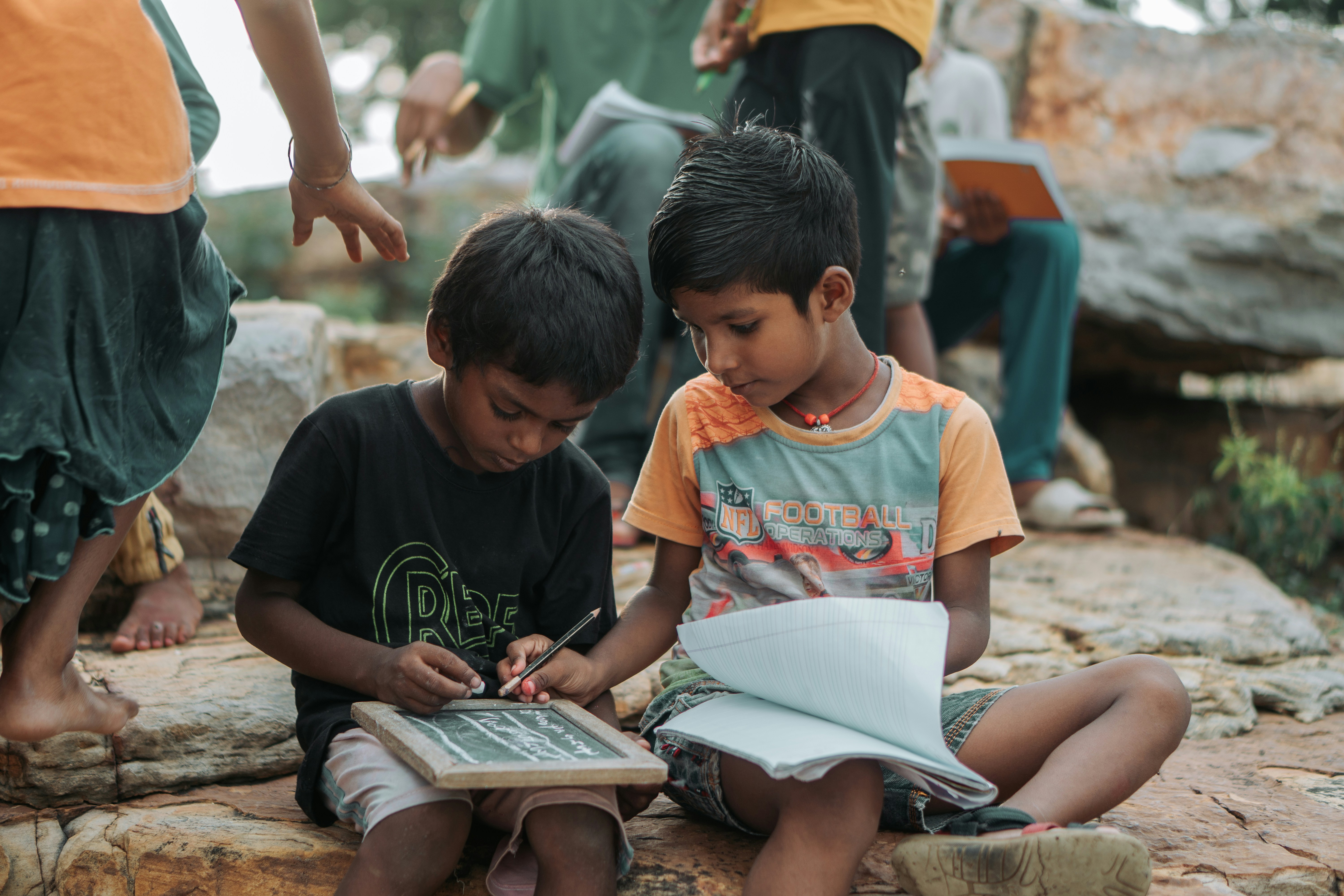 Two young boys learning outdoors with slate and notebook.