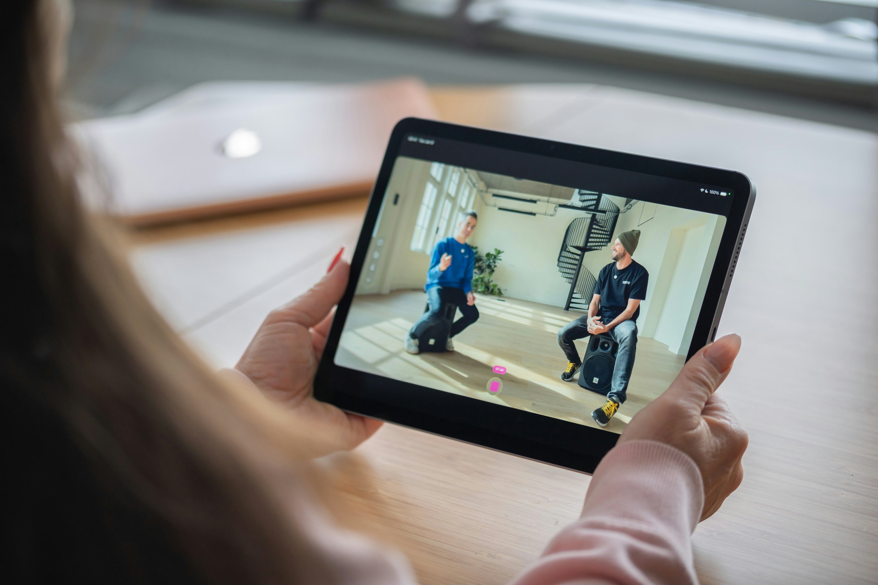 Person holding a tablet watching two men on screen.