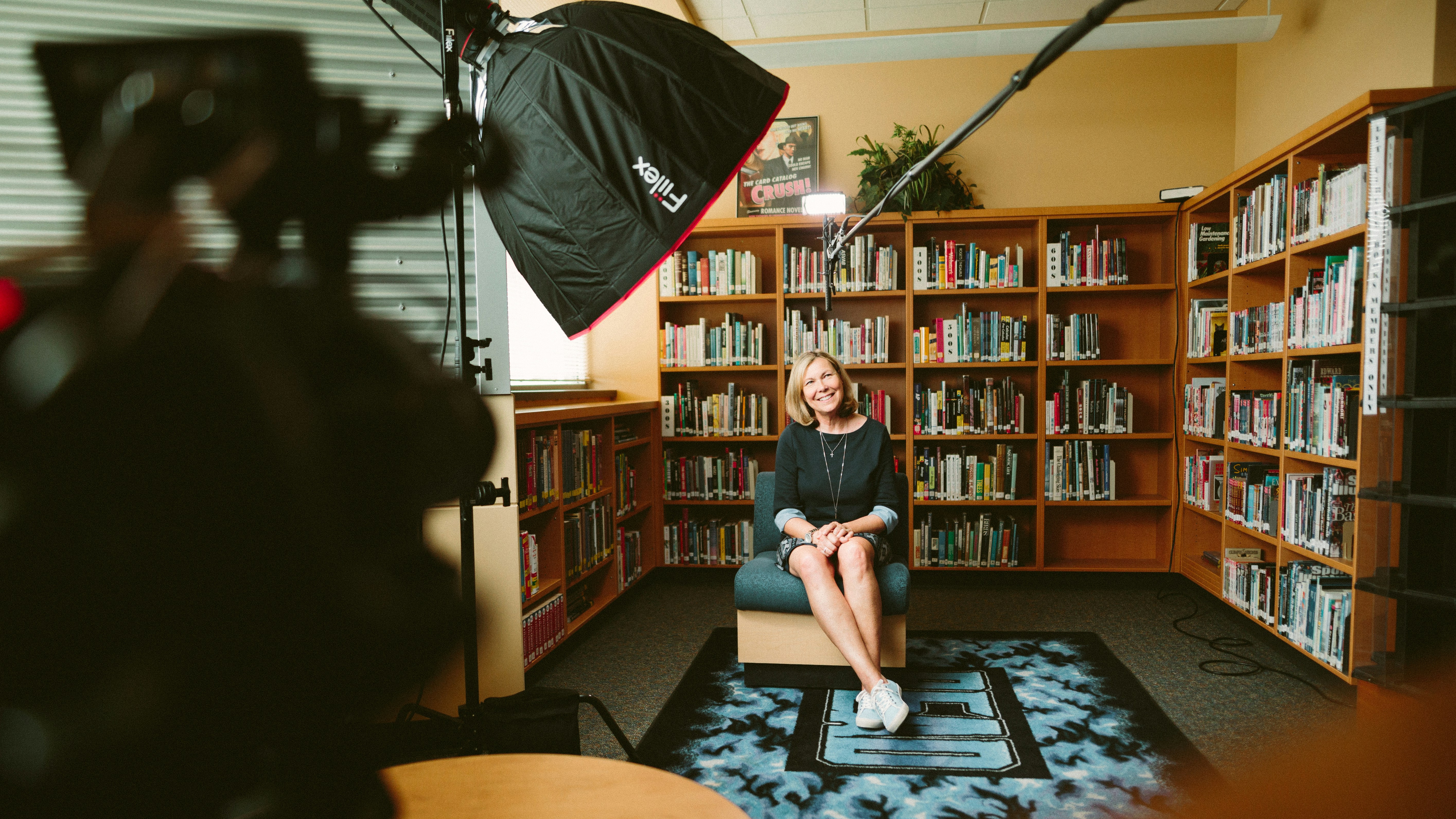 A snap shot from our film set while producing a documentary series for the Holocaust Center for Humanities. Here we are interviewing a local high school about their experience with some of the Center’s teaching materials. by School Play Scripts woman sitting on armless chair with light between bookcases in room