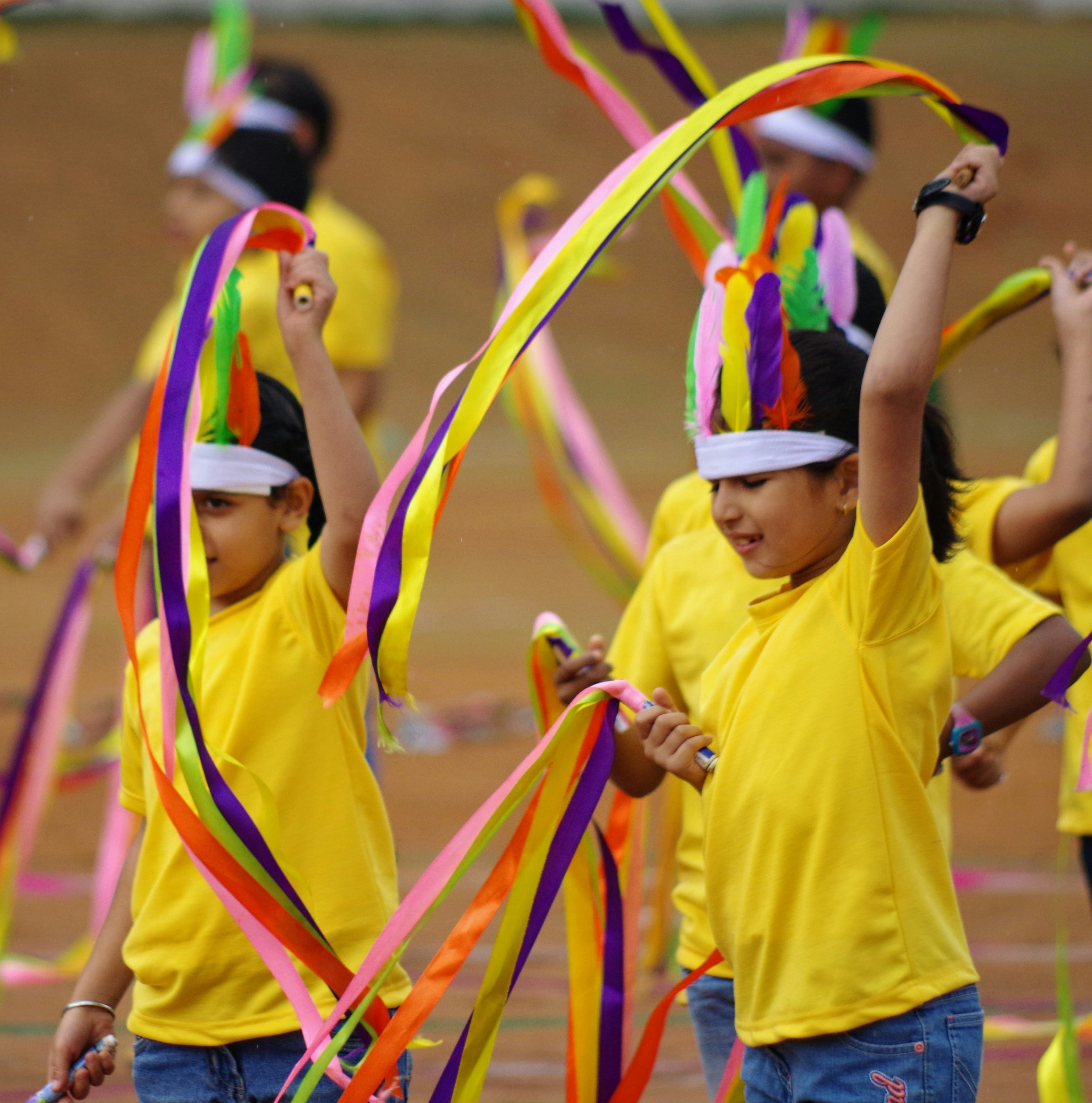 Kids putting on a show during an Independence Day celebration at a school in Bangalore, India. by School Play Scripts Children in yellow shirts dance with colorful ribbons