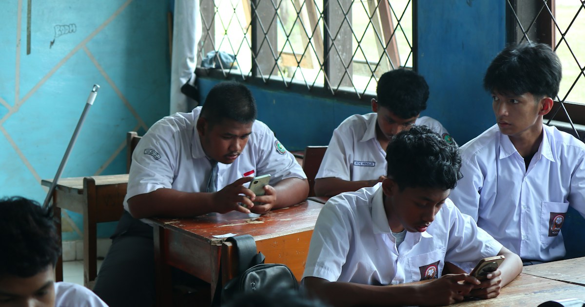 Students in uniform using phones in a classroom