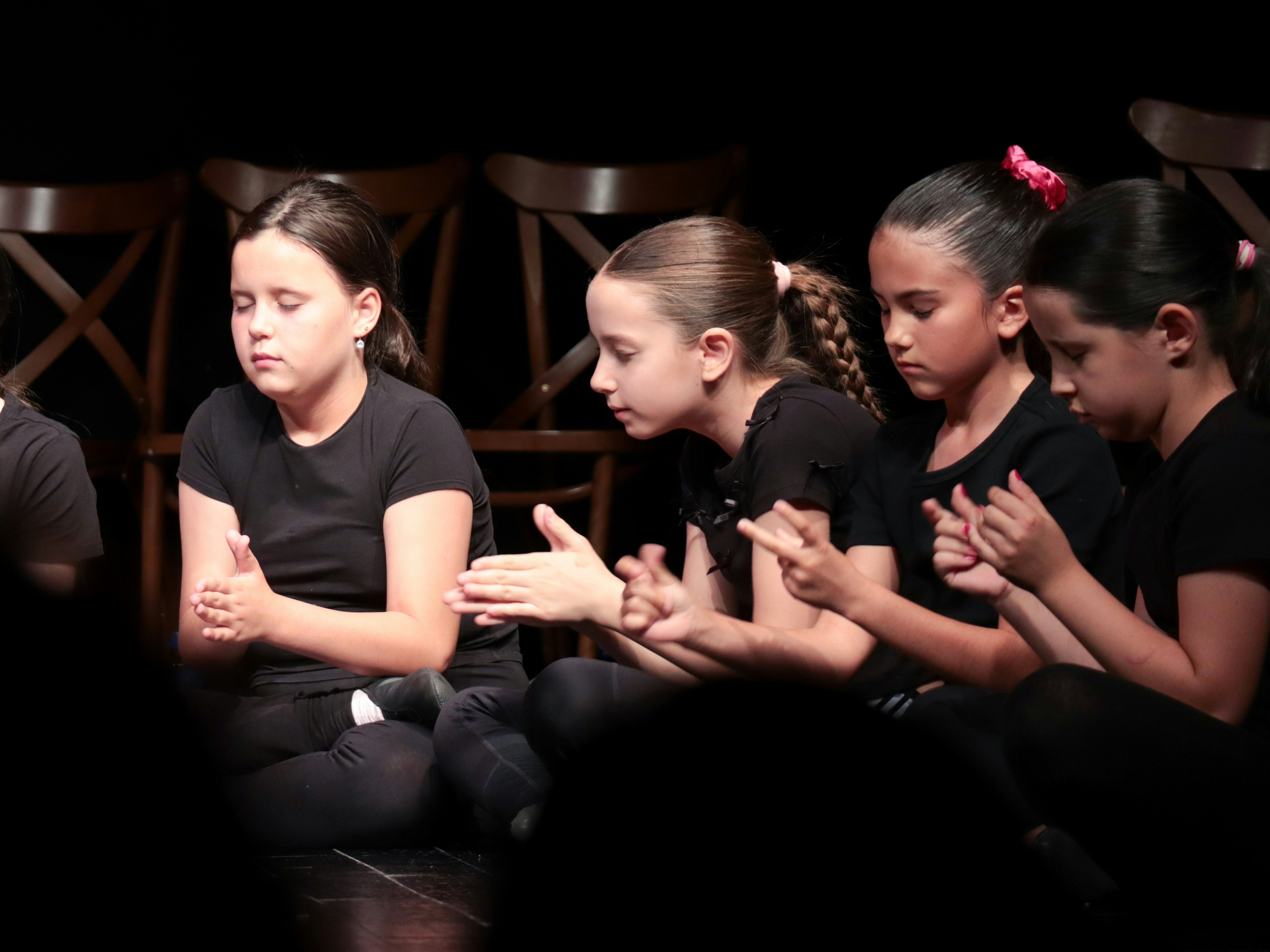 Frequently Asked Questions (FAQ) by School Play Scripts Four children in black clothing sitting on a stage with their hands together